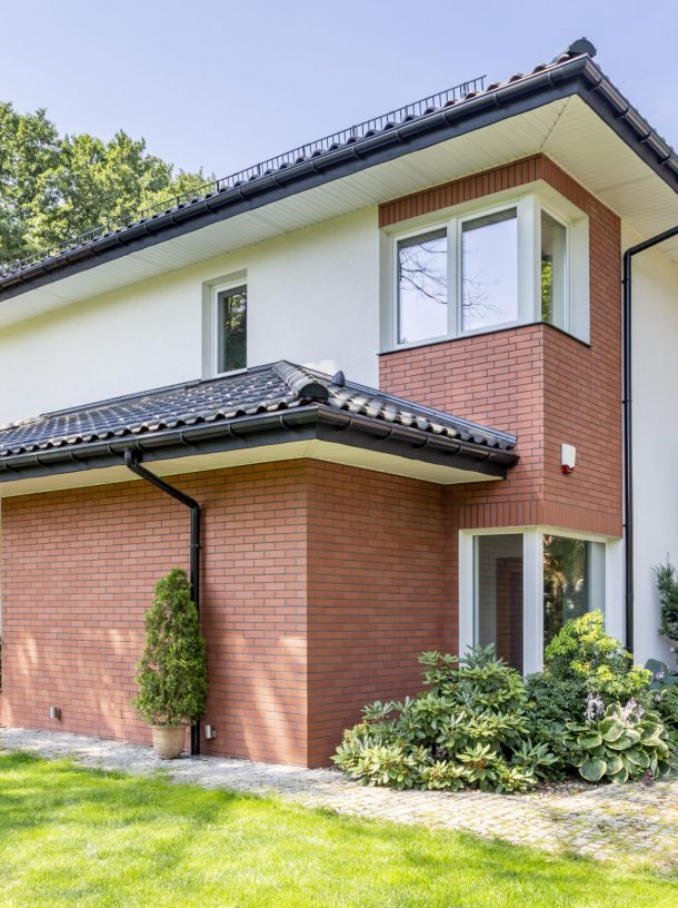 Red brick house with terrace and green grass and trees during summer
